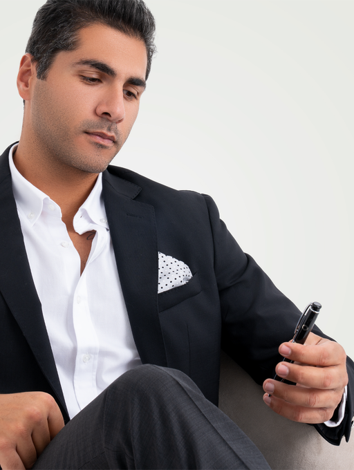  man in a black suit is sitting on a chair and looking at phone